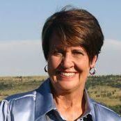 A woman in a blue shirt and earrings is smiling for the camera.