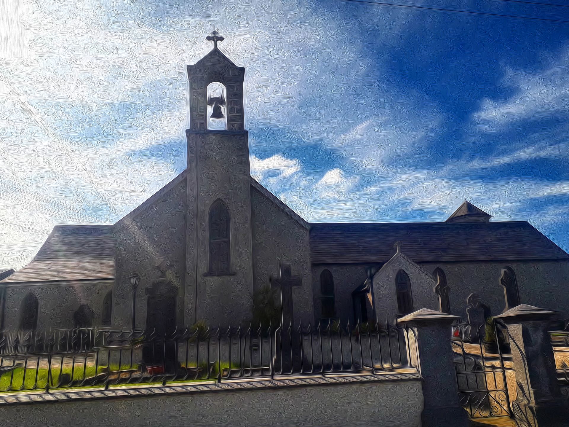 Stone church with bell tower and cross, seen behind a fence under a bright blue sky.
