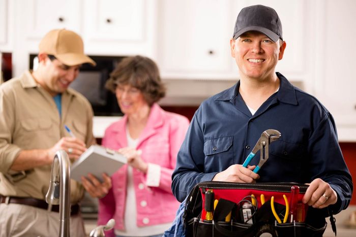 A Plumber Is Holding A Toolbox And Smiling In Front Of A Couple — Rome, GA — Crider Plumbing Co
