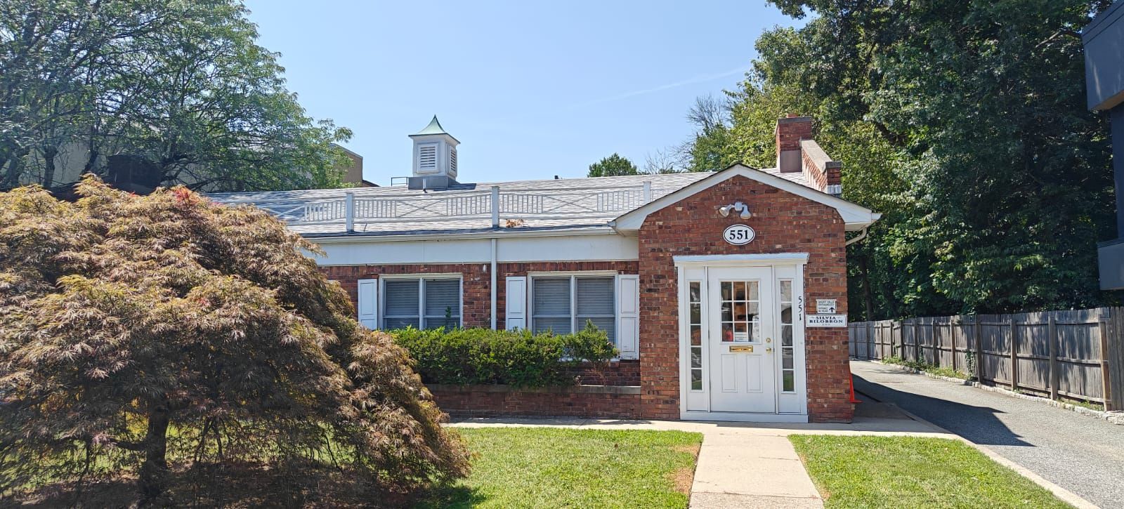 Red brick house with white trim, green lawn, and trees on a sunny day.