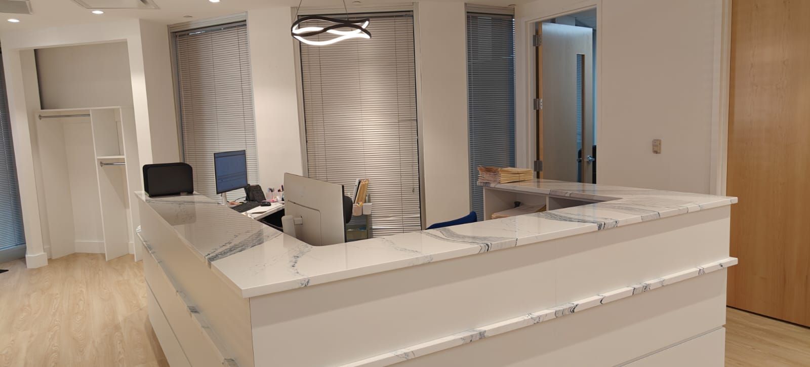 A modern office reception area with a white marble counter and a light wood floor.