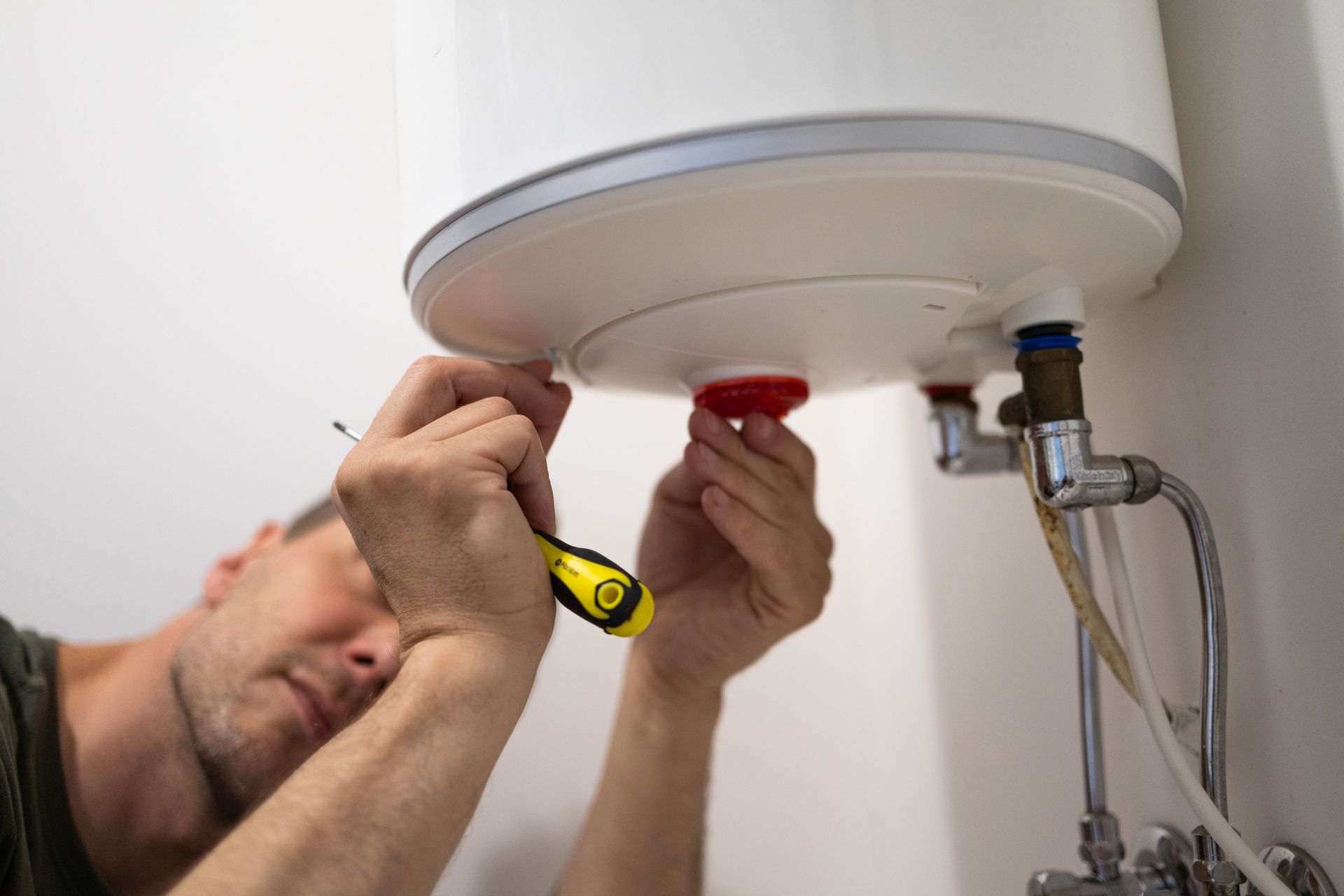 A plumber using a screwdriver to service a white electric water heater