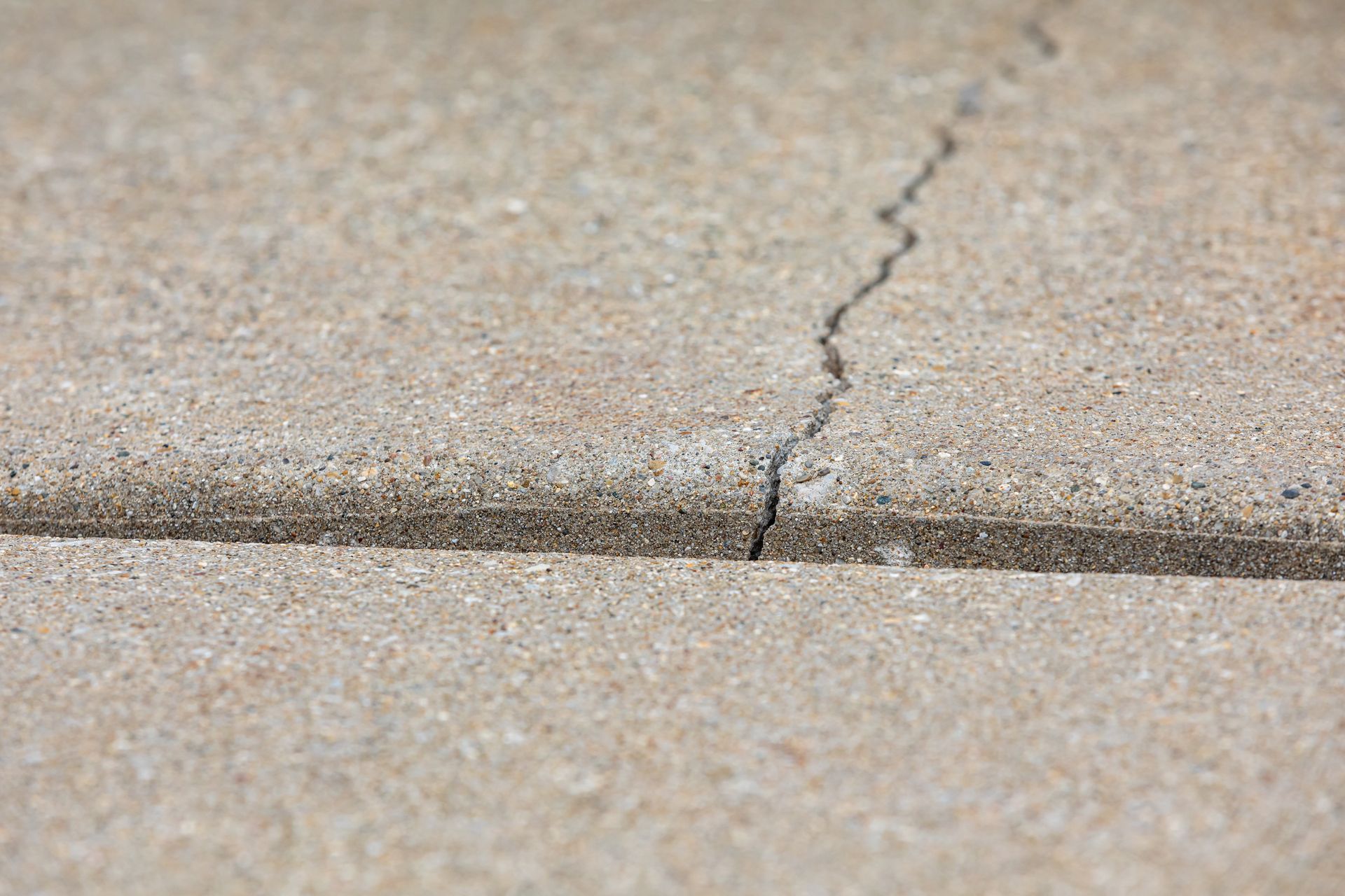 Cracked concrete driveway slabs with a visible gap between uneven panels. Cracked concrete driveway slabs with a visible gap between uneven panels.