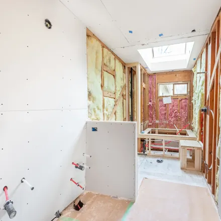 Bathroom renovation in progress: exposed framing, insulation, drywall, skylight, and a built-in tub frame.