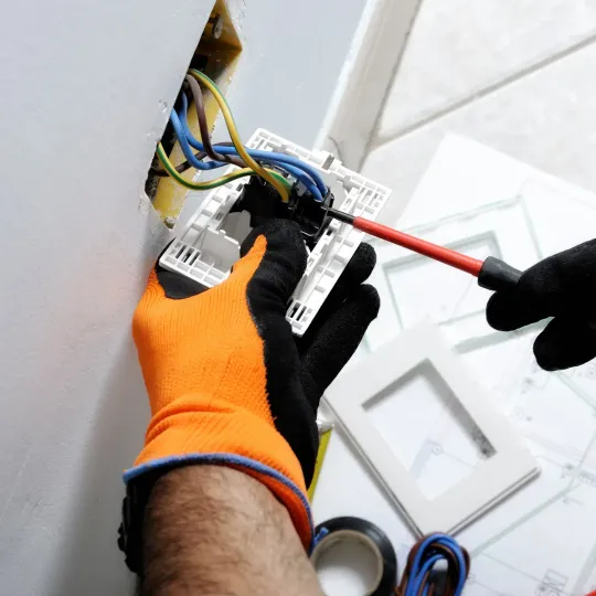 Electrician in orange vest working on electrical outlet.