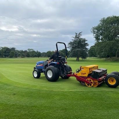 A man is driving a tractor on a golf course.