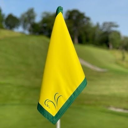 A yellow golf flag with a green border is on a golf course.