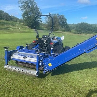 A blue lawn mower with a conveyor belt attached to it is parked on a golf course.