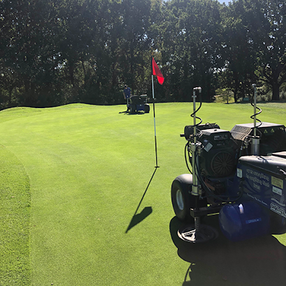 A lawn mower is parked on a golf course next to a flag