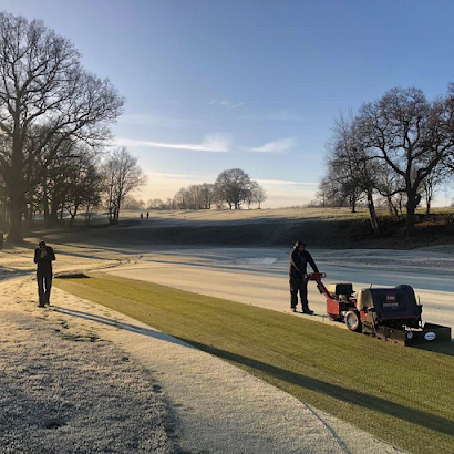 A man is pushing a lawn mower on a golf course