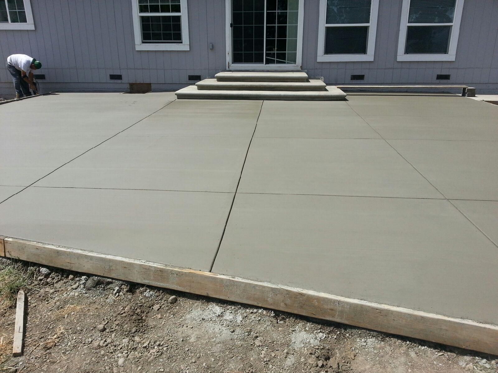 A man is working on a concrete patio in front of a house.