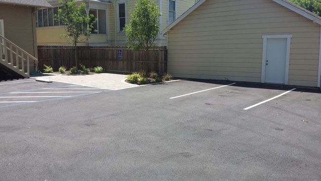 A parking lot with a house in the background and a garage in the foreground.