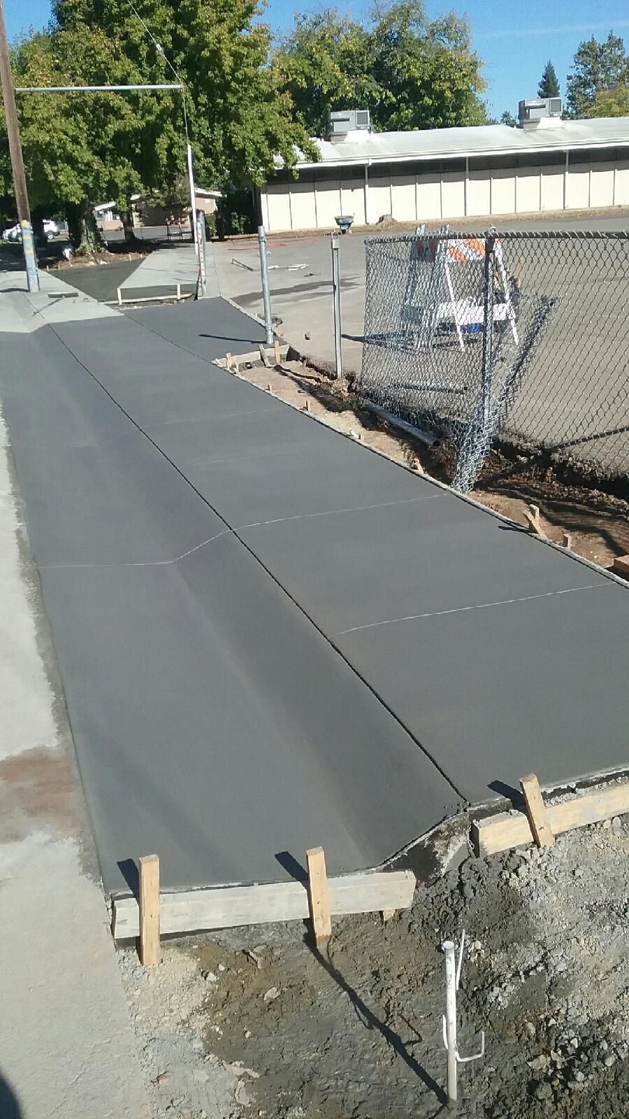 A concrete walkway is being built next to a chain link fence.