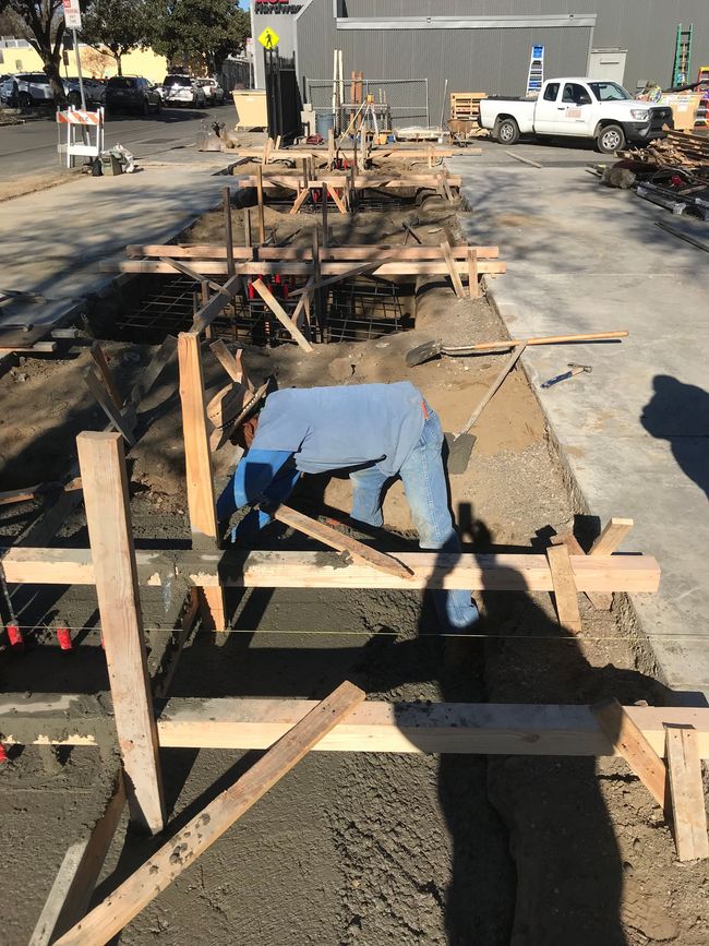 A construction worker is laying concrete on a sidewalk.