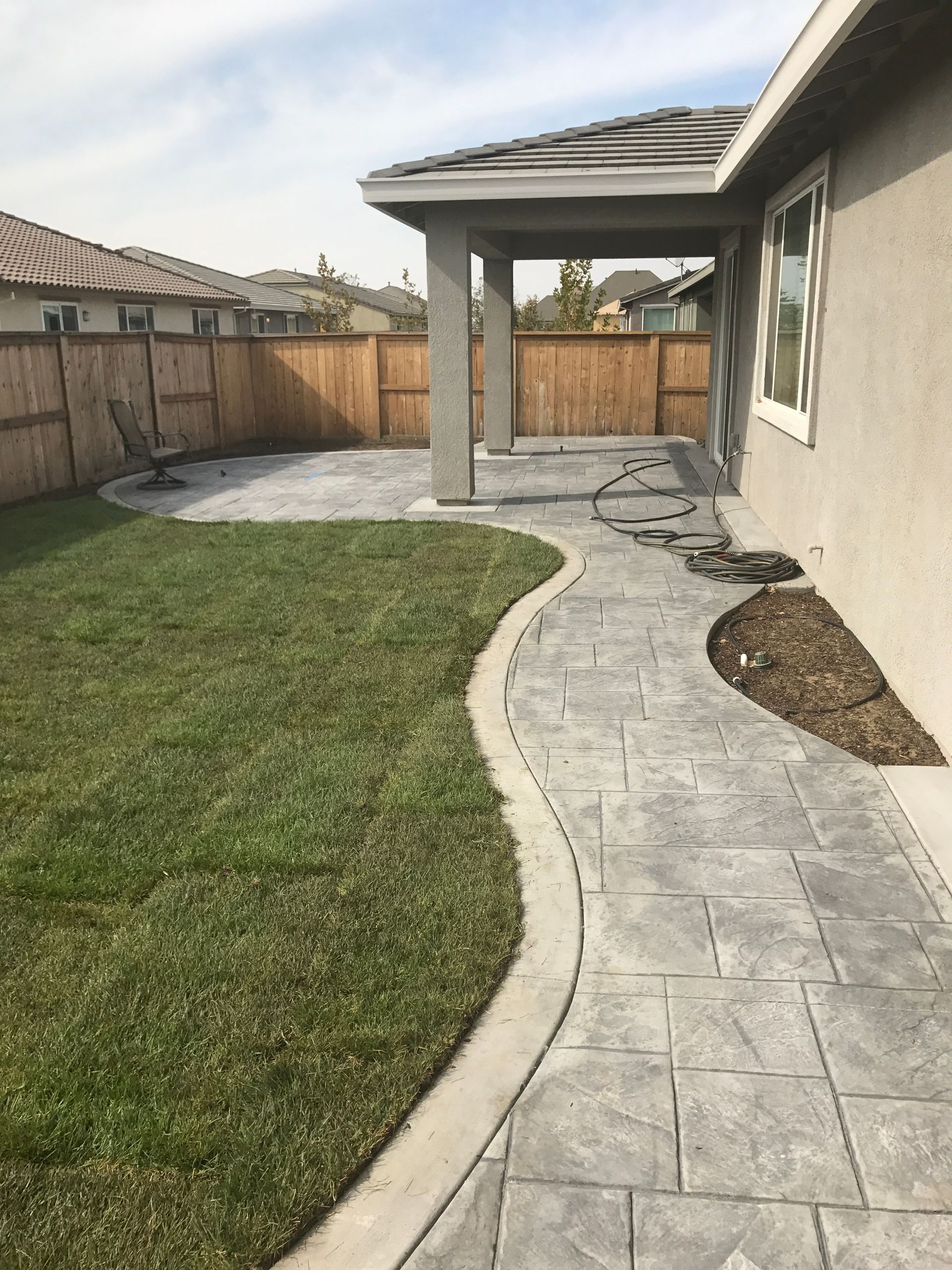 A concrete walkway leading to a covered patio in the backyard of a house.