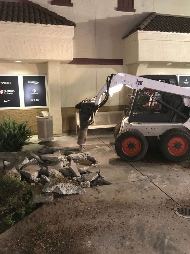 A bobcat is being used to demolish a sidewalk in front of a building.