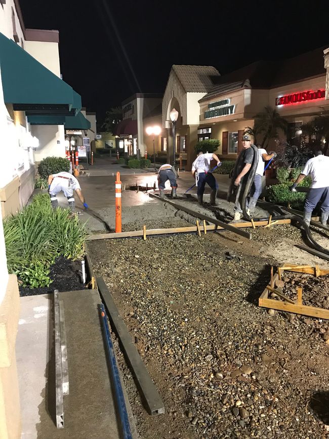 A group of people are working on a sidewalk at night.