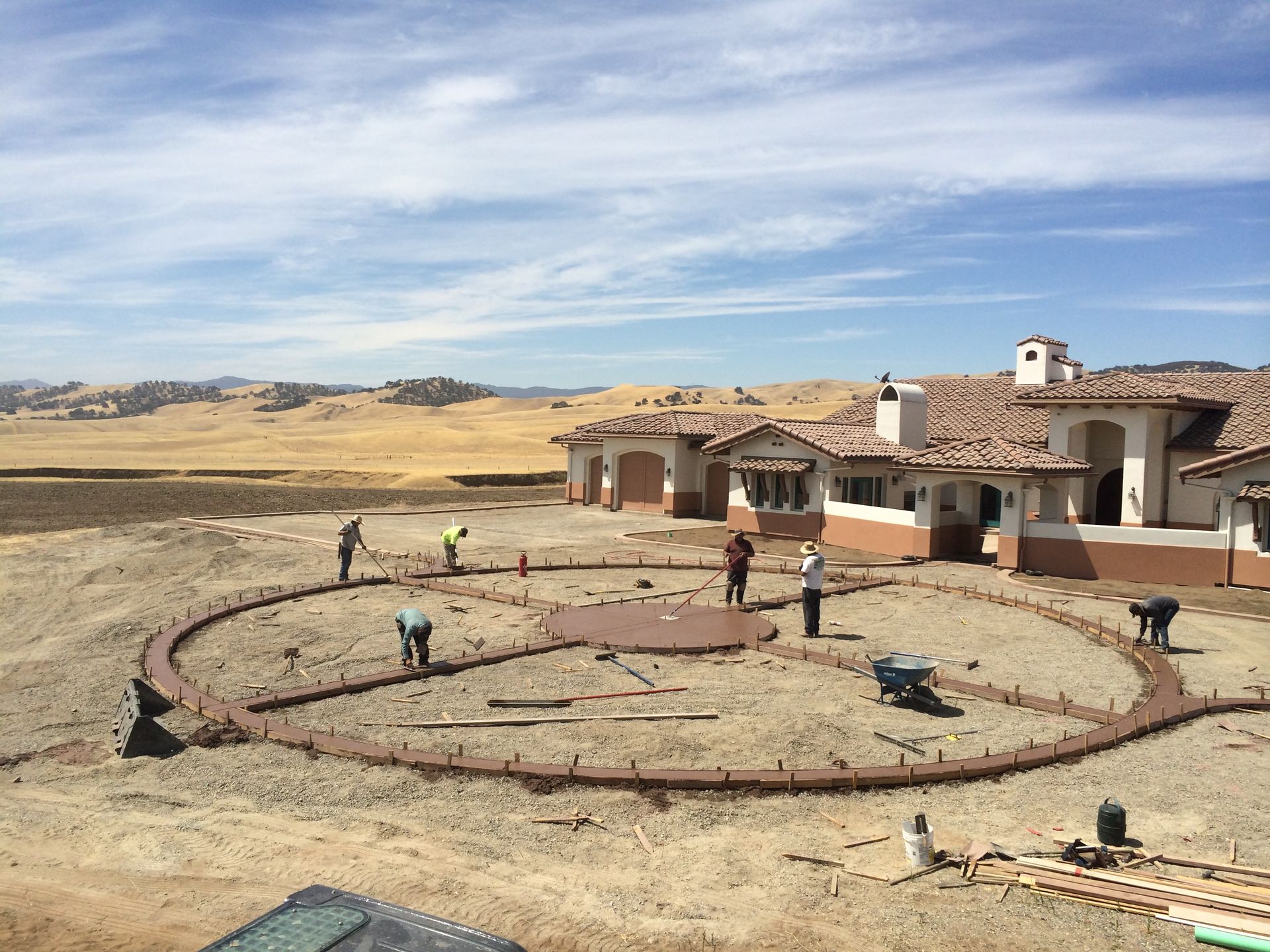 A group of people are working on a concrete circle in front of a large house.