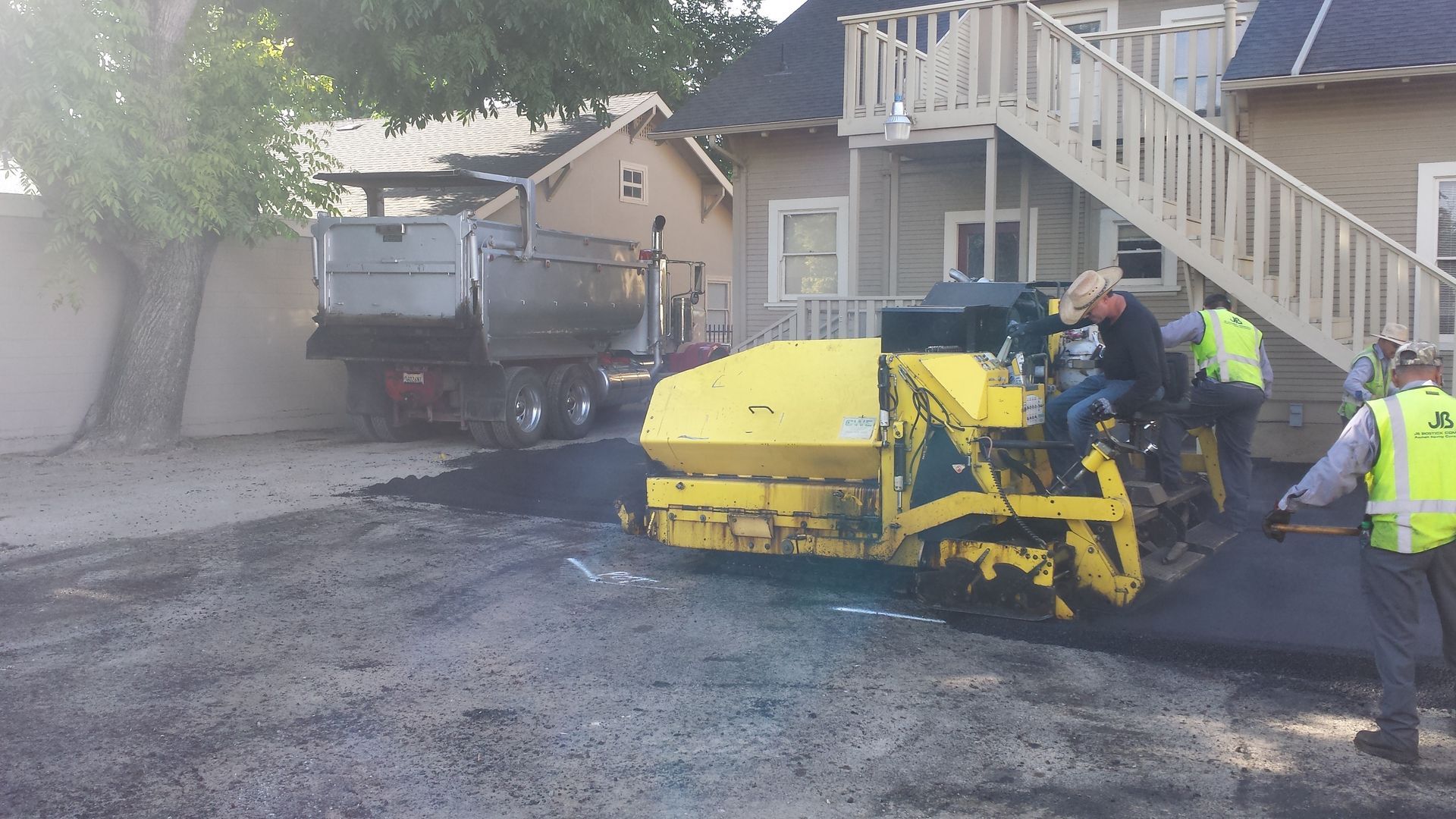 A group of construction workers are working on a driveway in front of a house.