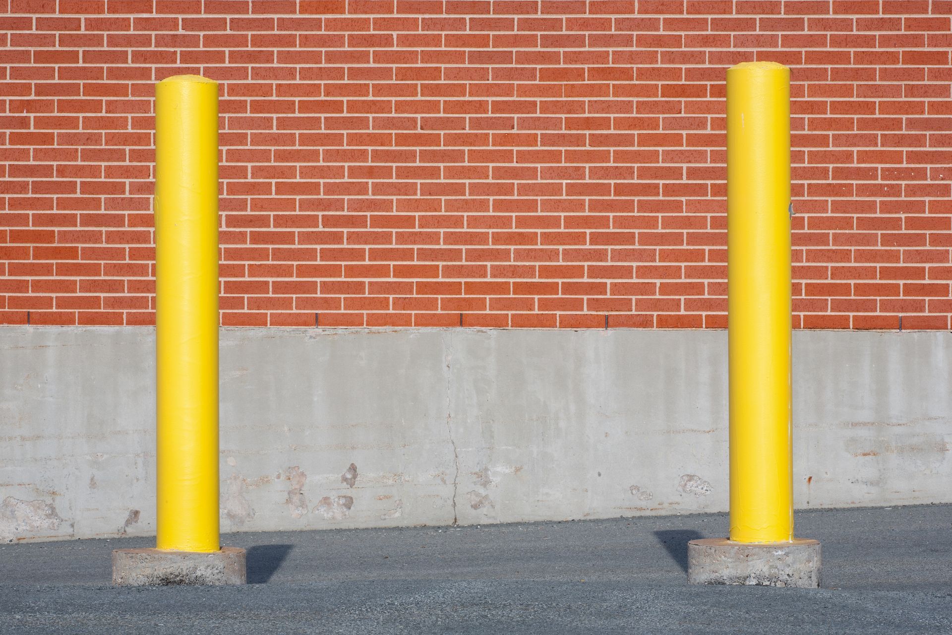 Two yellow bollards in front of a brick wall