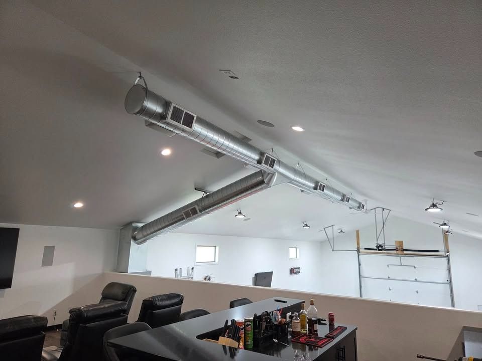 Modern lounge with reclining chairs, bar counter, and exposed silver ventilation ducts on a white ceiling