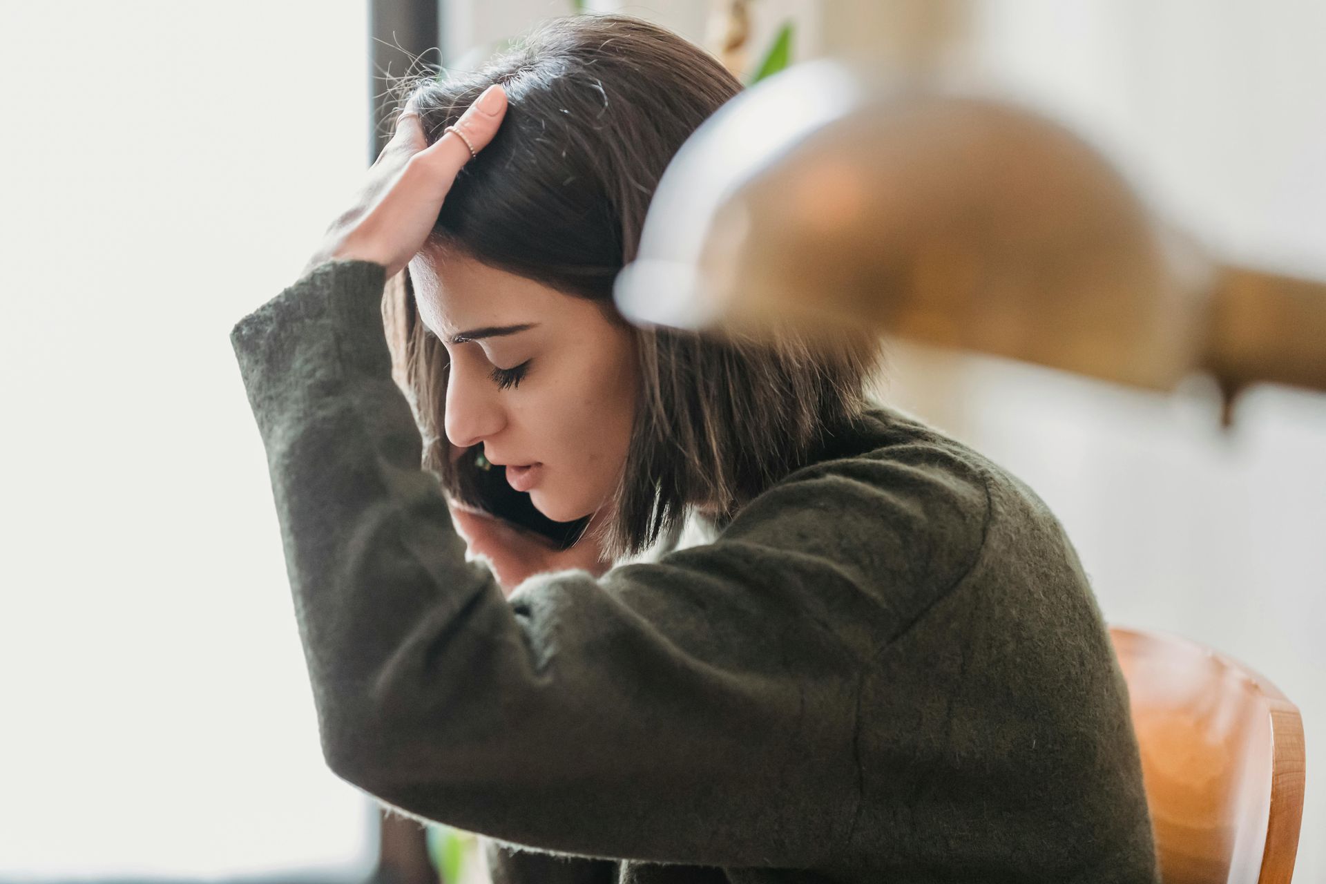 Woman on the phone, holding her head at a desk, looking stressed or tired.