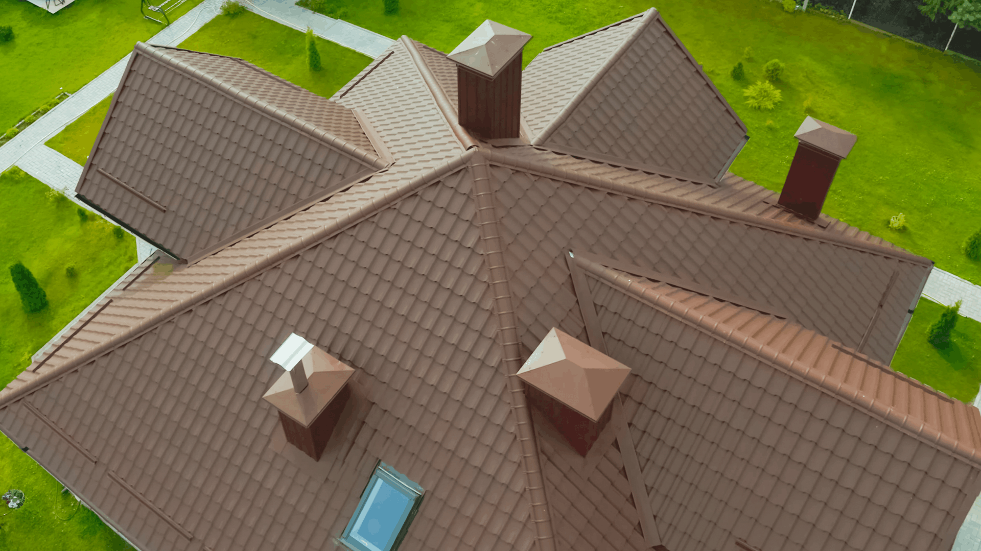 Brown tiled roof of a house with several chimneys, set against green grass — C&A Roofing In Boambee East, NSW