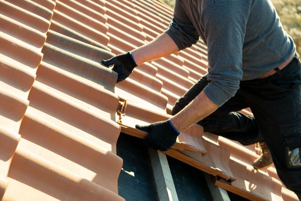 Person in Black Gloves Installing Clay Roof Tiles on a Sunny Day — C&A Roofing In Tamworth, NSW