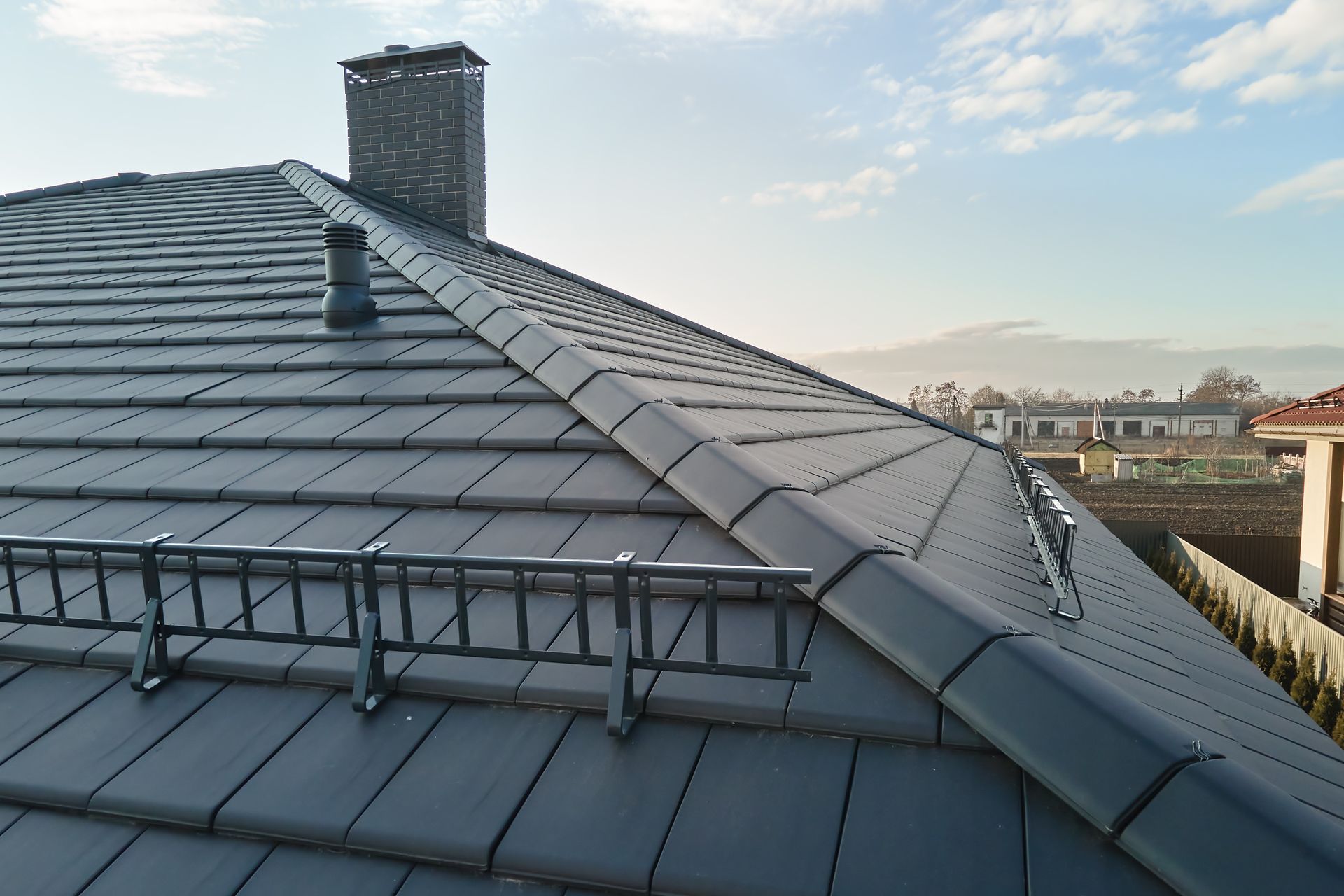 Dark Gray Tiled Roof With a Ladder and Chimney Against a Blue Sky — C&A Roofing In Taree, NSW