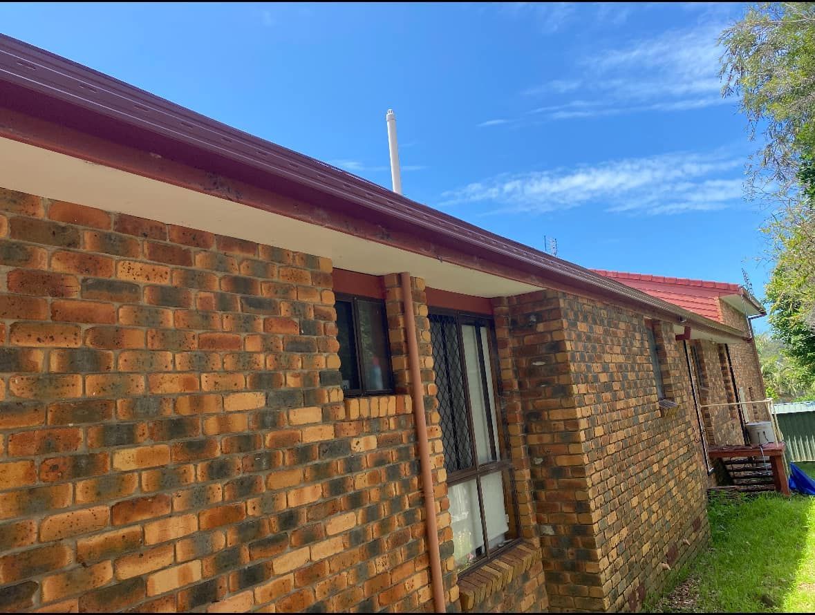 Brick house exterior with red roof trim, blue sky — C&A Roofing in Boambee East, NSW