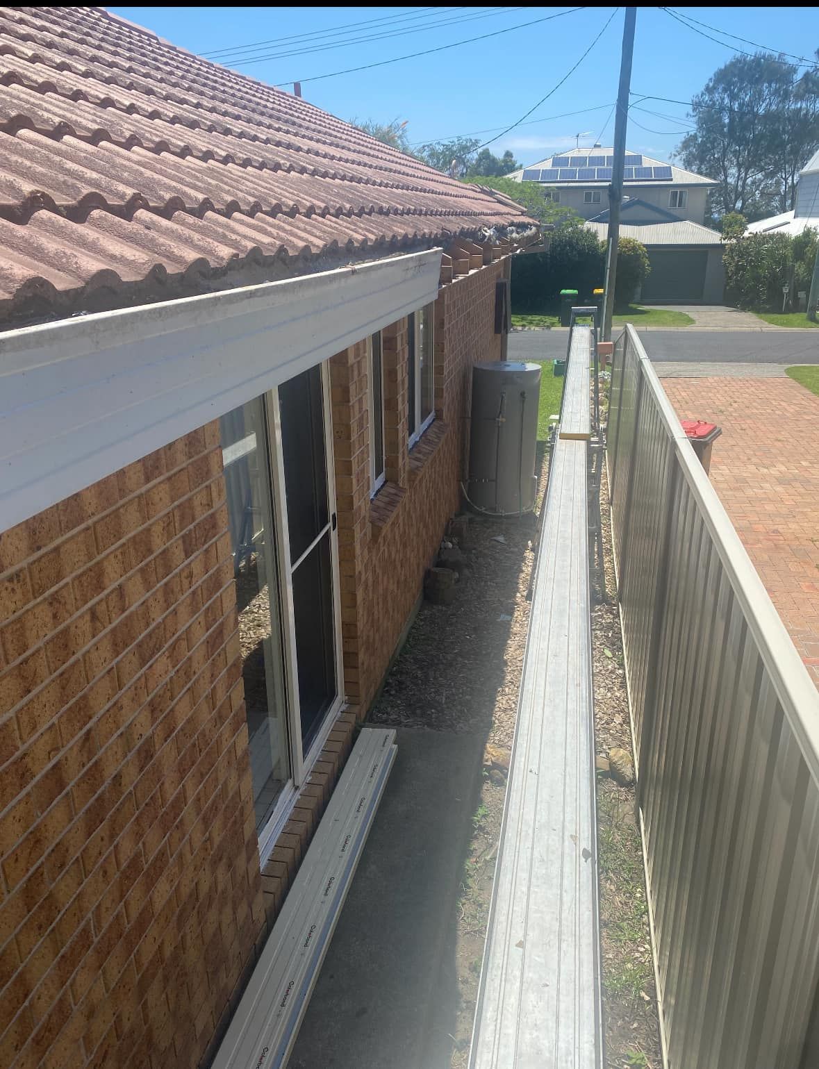 Brick house with red-tiled roof, white gutters, and a narrow walkway alongside a fence.