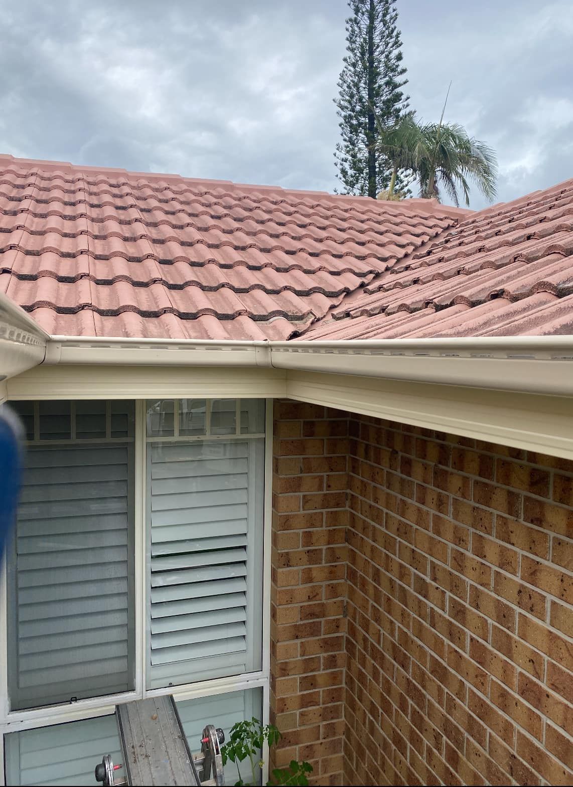 Red tile roof and white gutters on a brick home with closed window shutters.