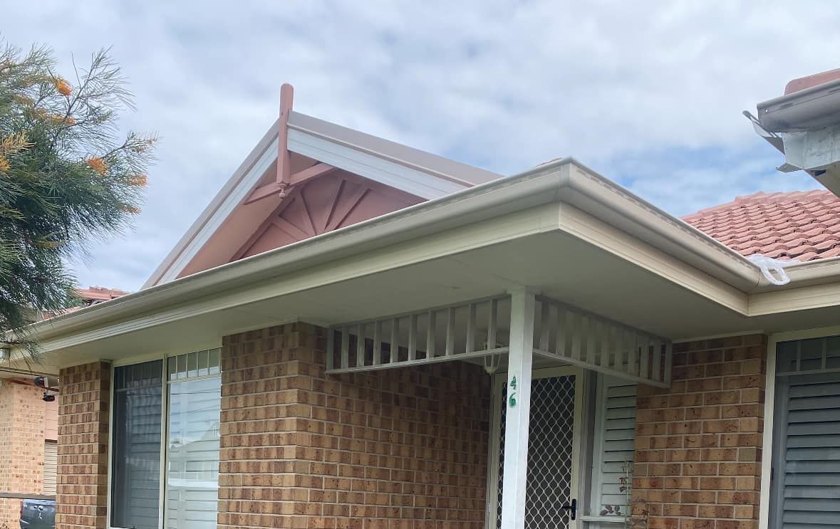 Brick house with a red-tiled roof, beige trim, and a small porch. Overcast sky.