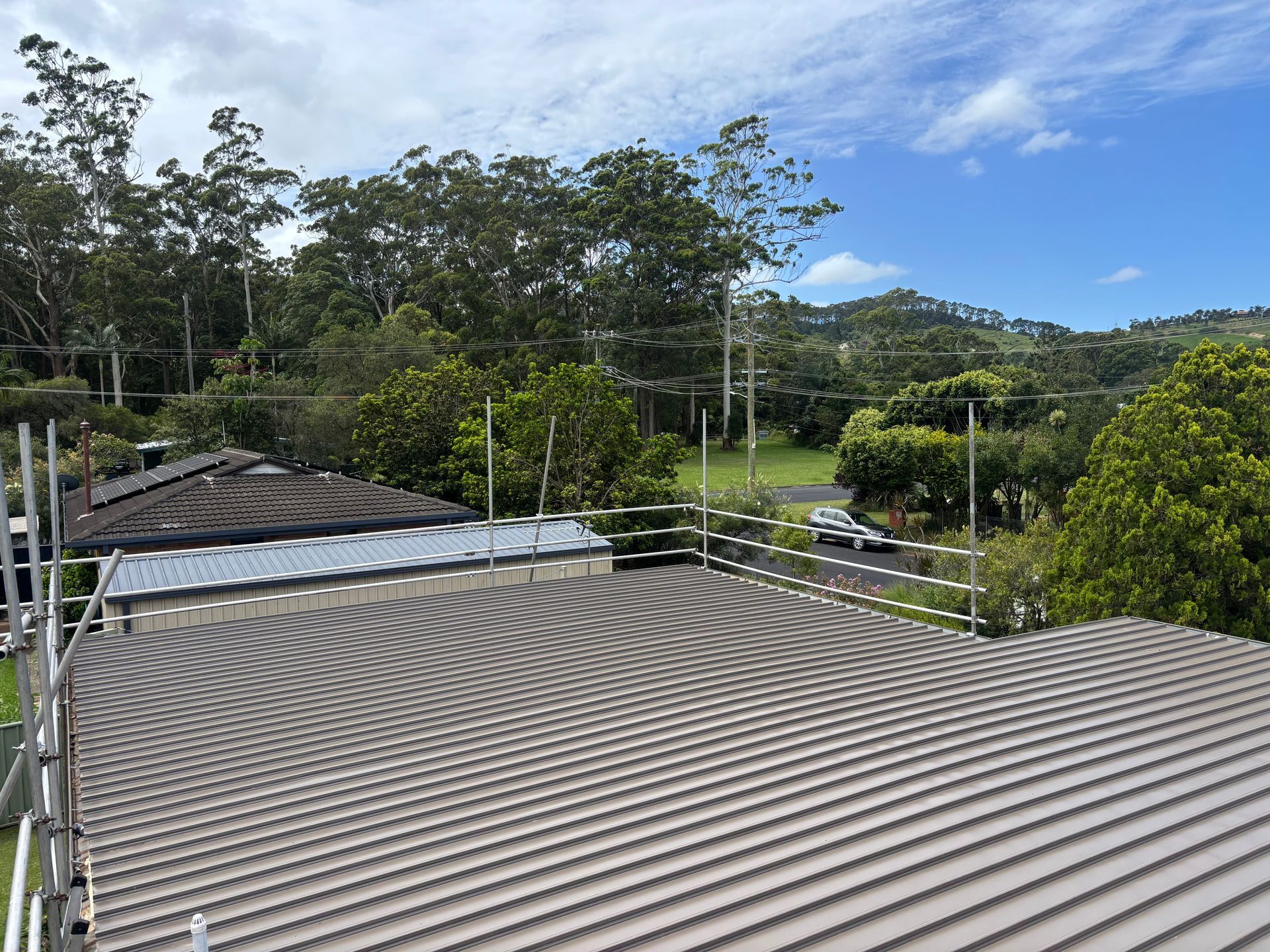 Metal roof with safety railings, trees, a road, and a cloudy sky.