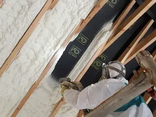 A man is spraying foam on the ceiling of a building.