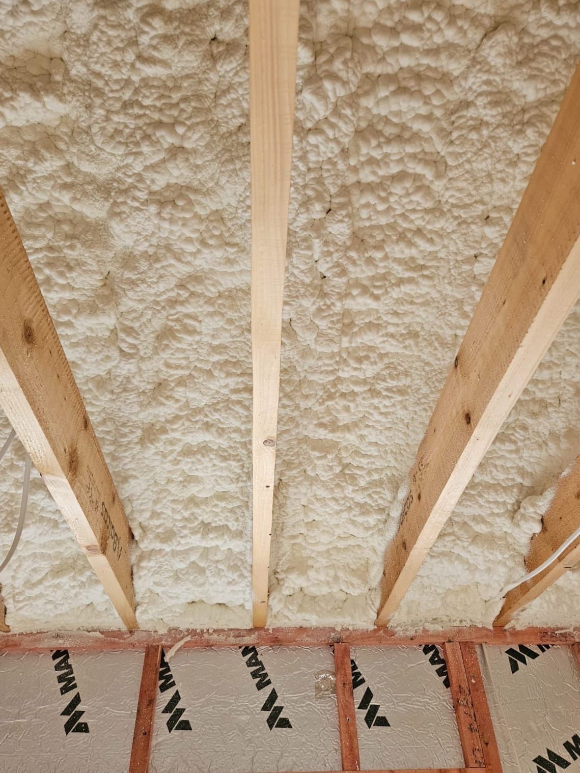 A close up of a ceiling with foam insulation and wooden beams.