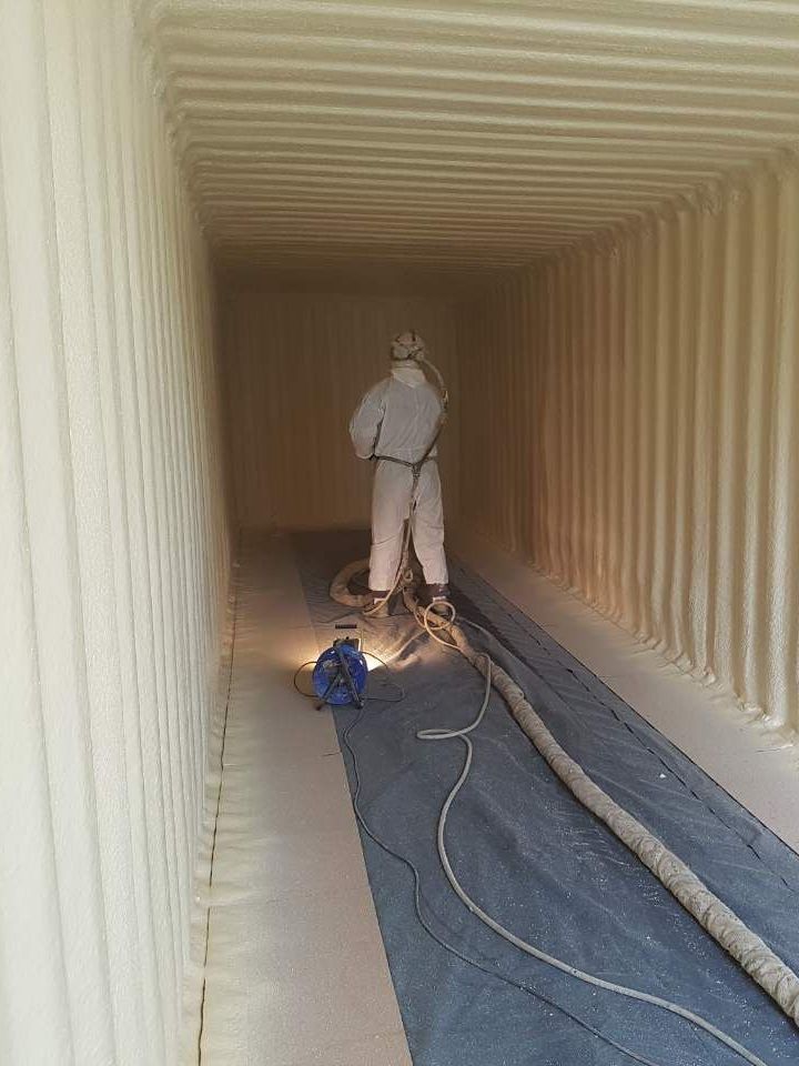 A man is spraying foam on the floor of a shipping container.