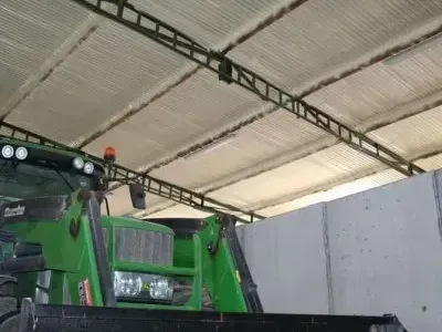 A green tractor is parked in a warehouse under a roof.