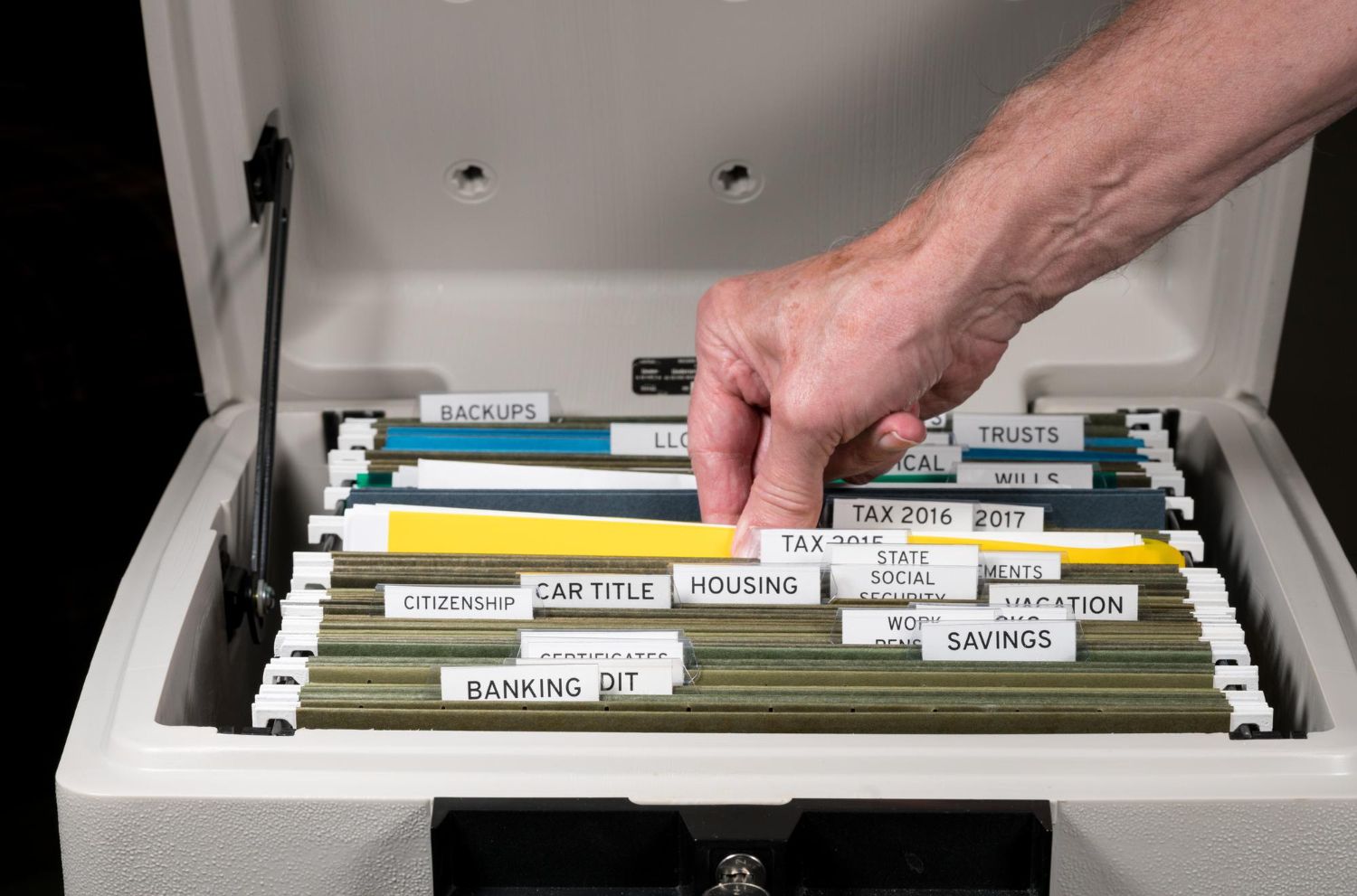 Hand reaching into a gray fire-resistant file cabinet, selecting a yellow file.