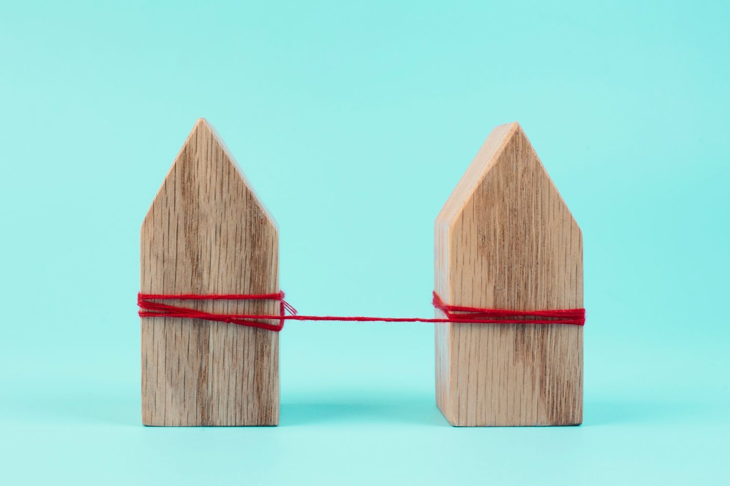 Two wooden house models connected by red string against a teal background.
