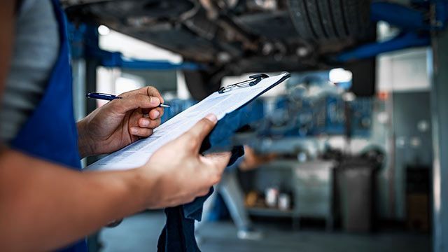 A Mechanic Is Writing On A Clipboard In A Garage — Manning Smash & Auto Repairs In Wingham, NSW