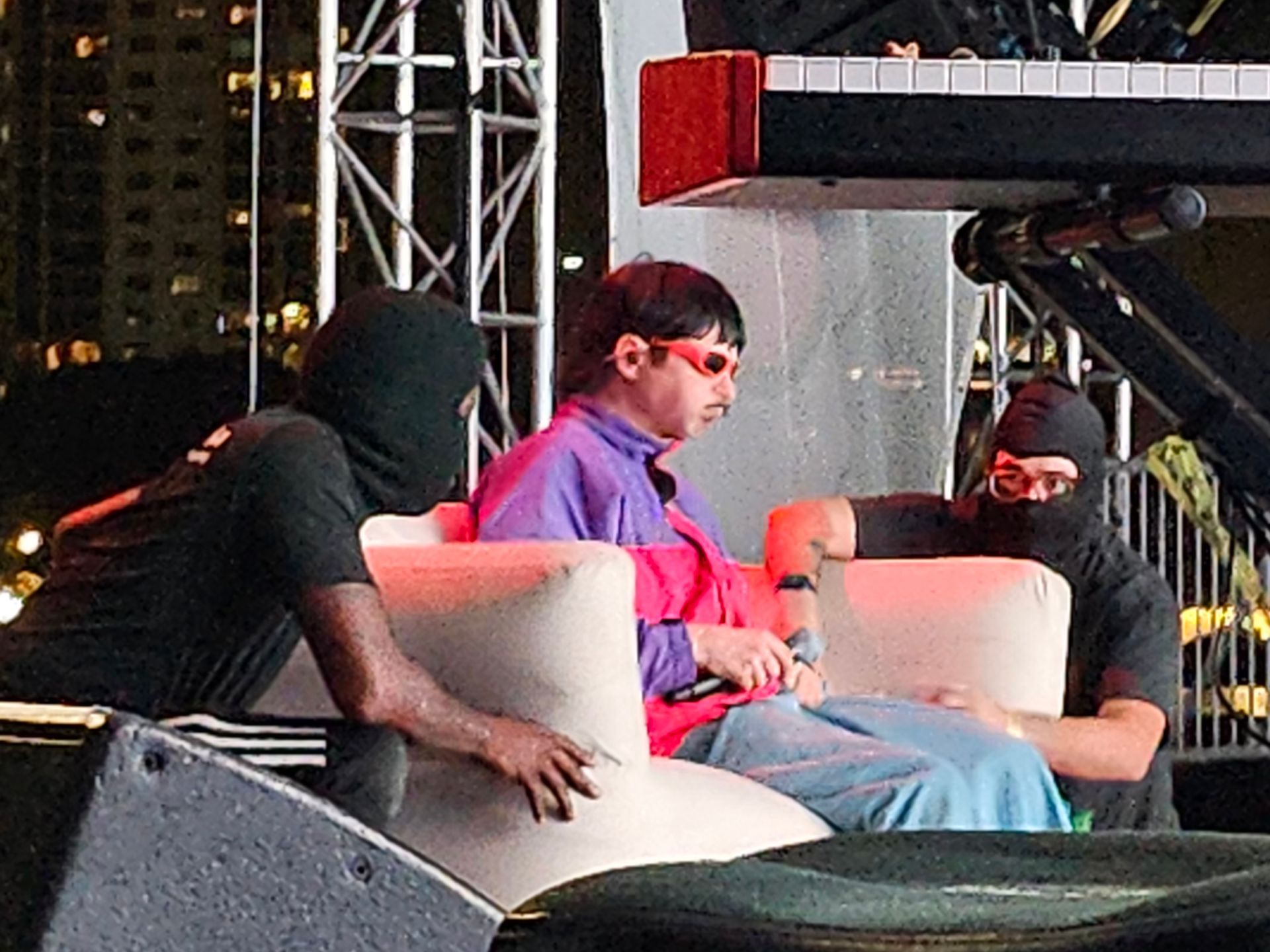 A group of men are sitting in chairs on a stage with a piano in the background.