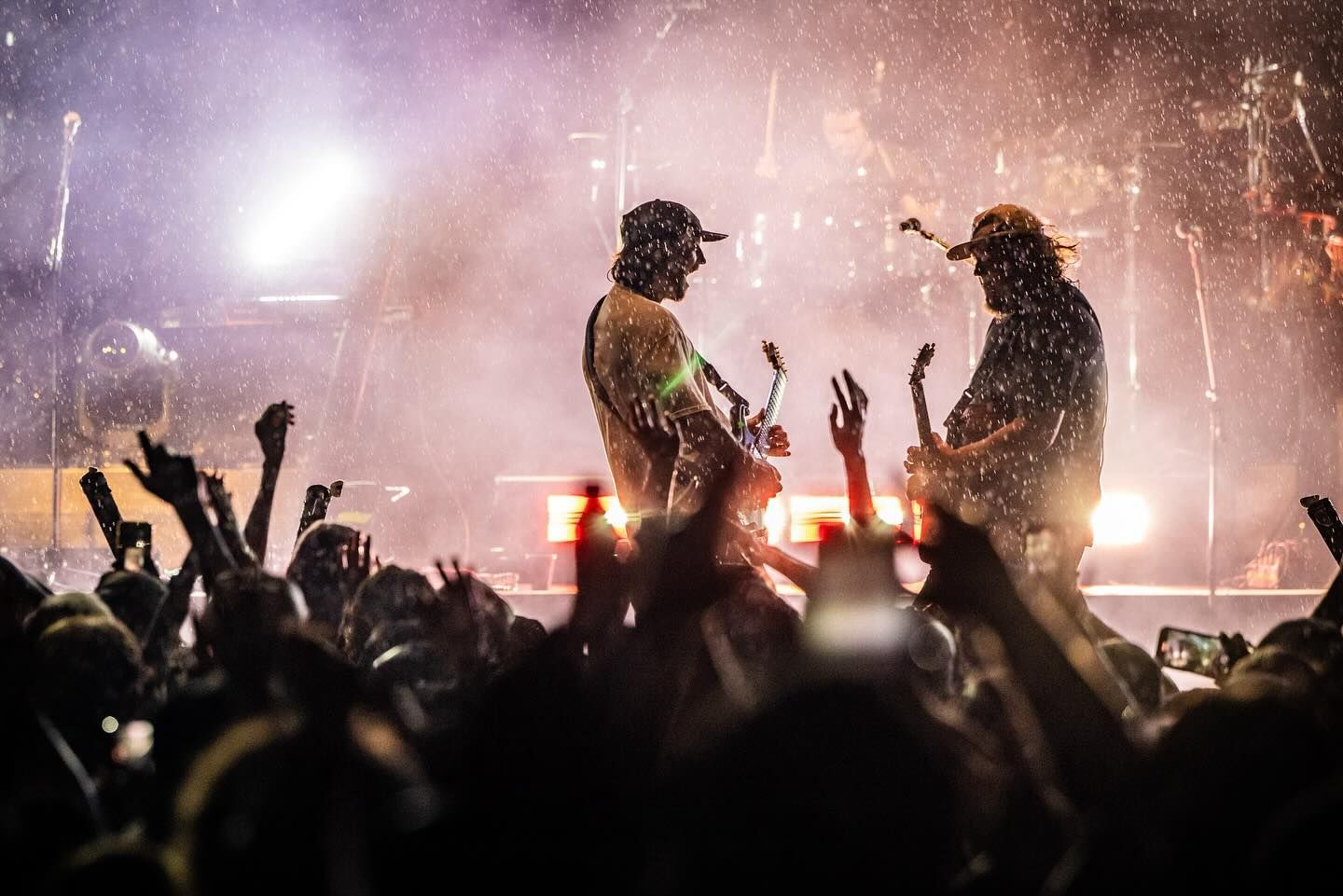 Two men are playing guitars in front of a crowd at a concert.