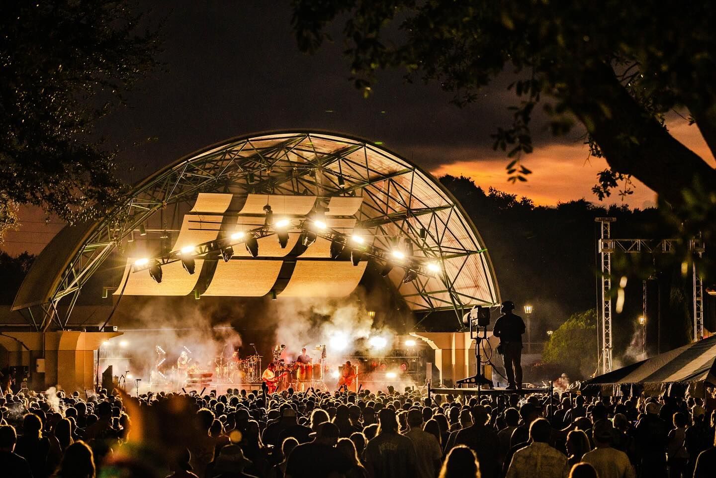 A large crowd of people are watching a concert at night.