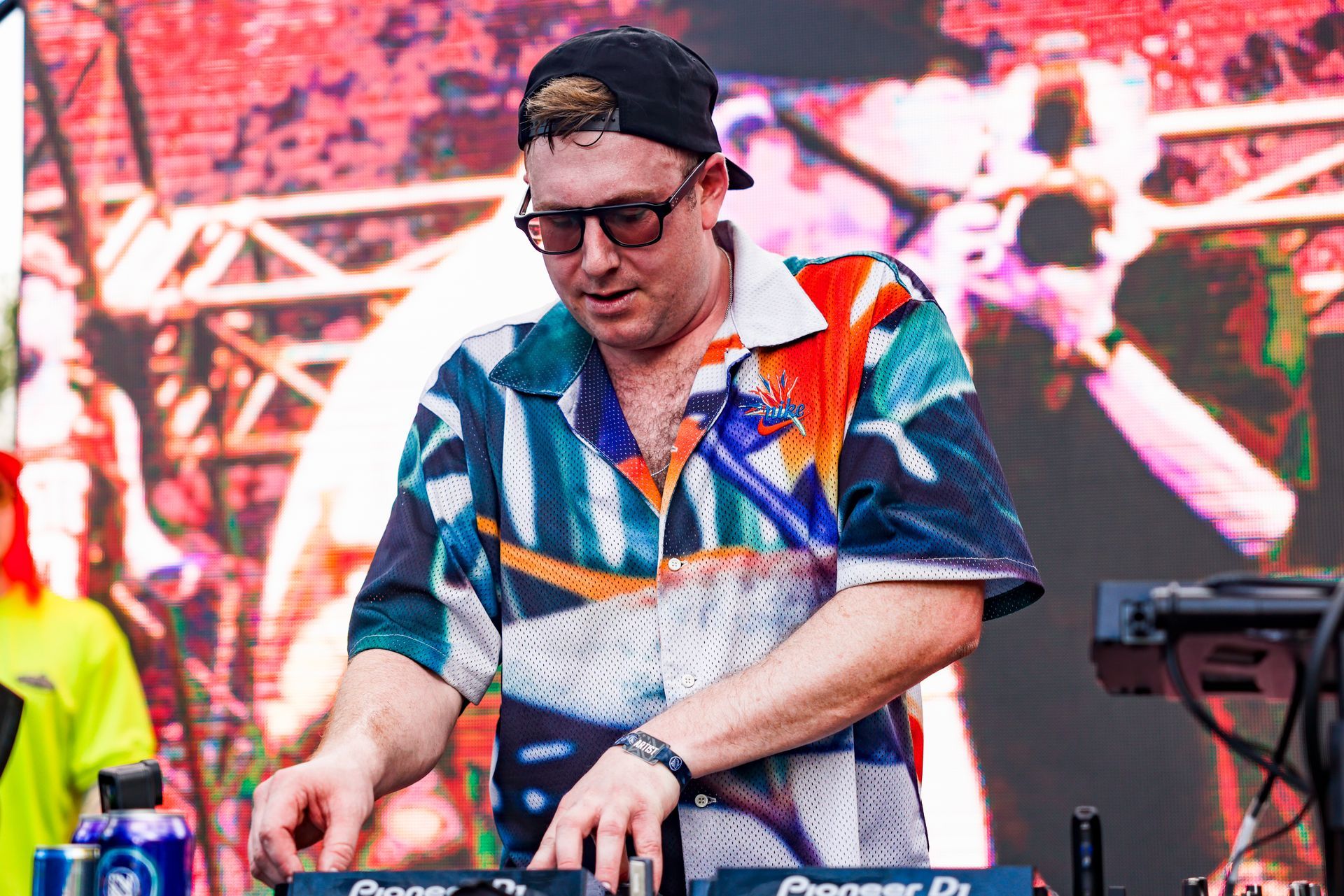 A man wearing sunglasses and a hat is playing a dj set on a stage.