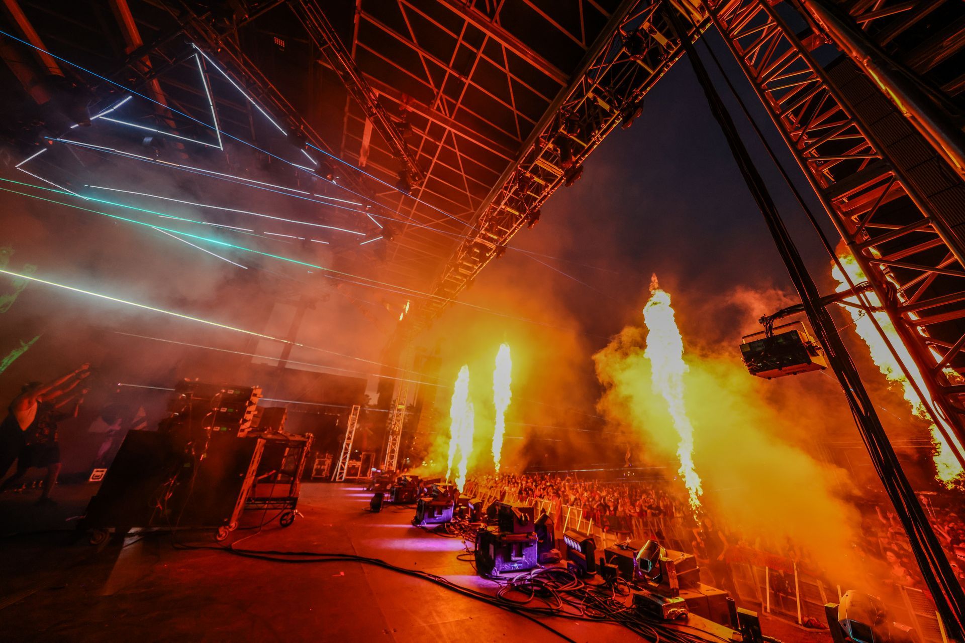 A crowd of people are watching a concert with fire coming out of the ceiling.