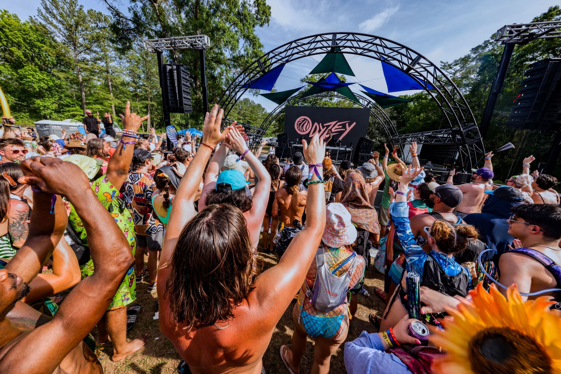 A crowd of people are dancing at a festival with their hands in the air.