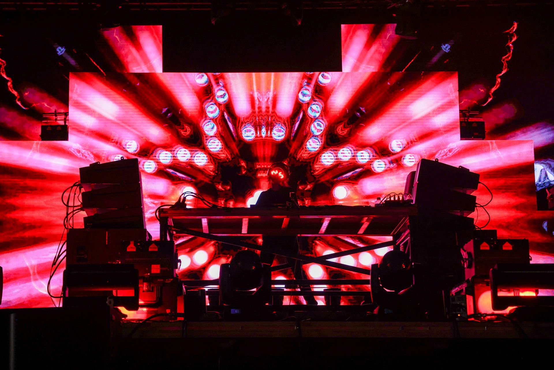A dj is playing music on a stage with a large screen behind him.