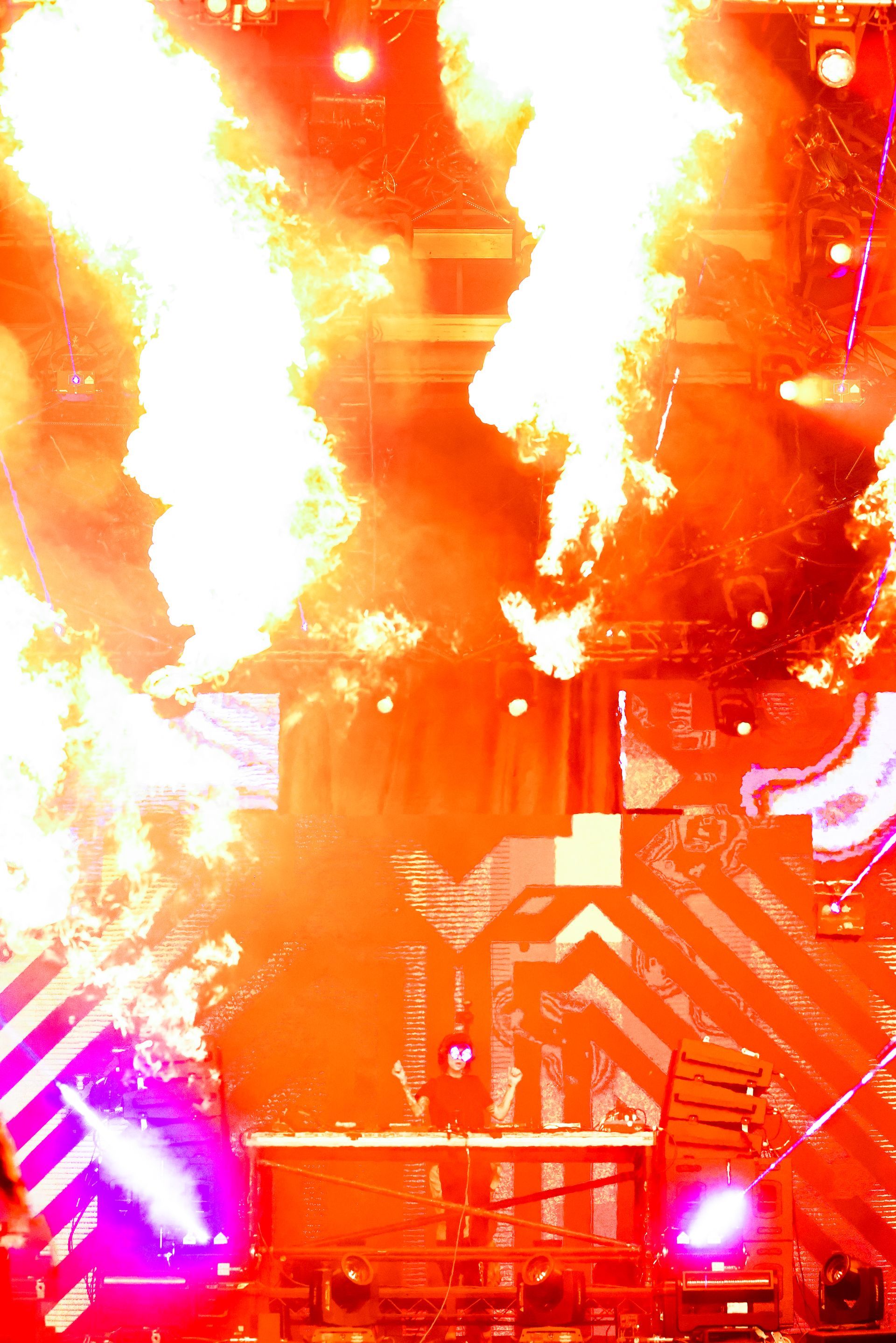 A dj is playing music on a stage with flames coming out of it.