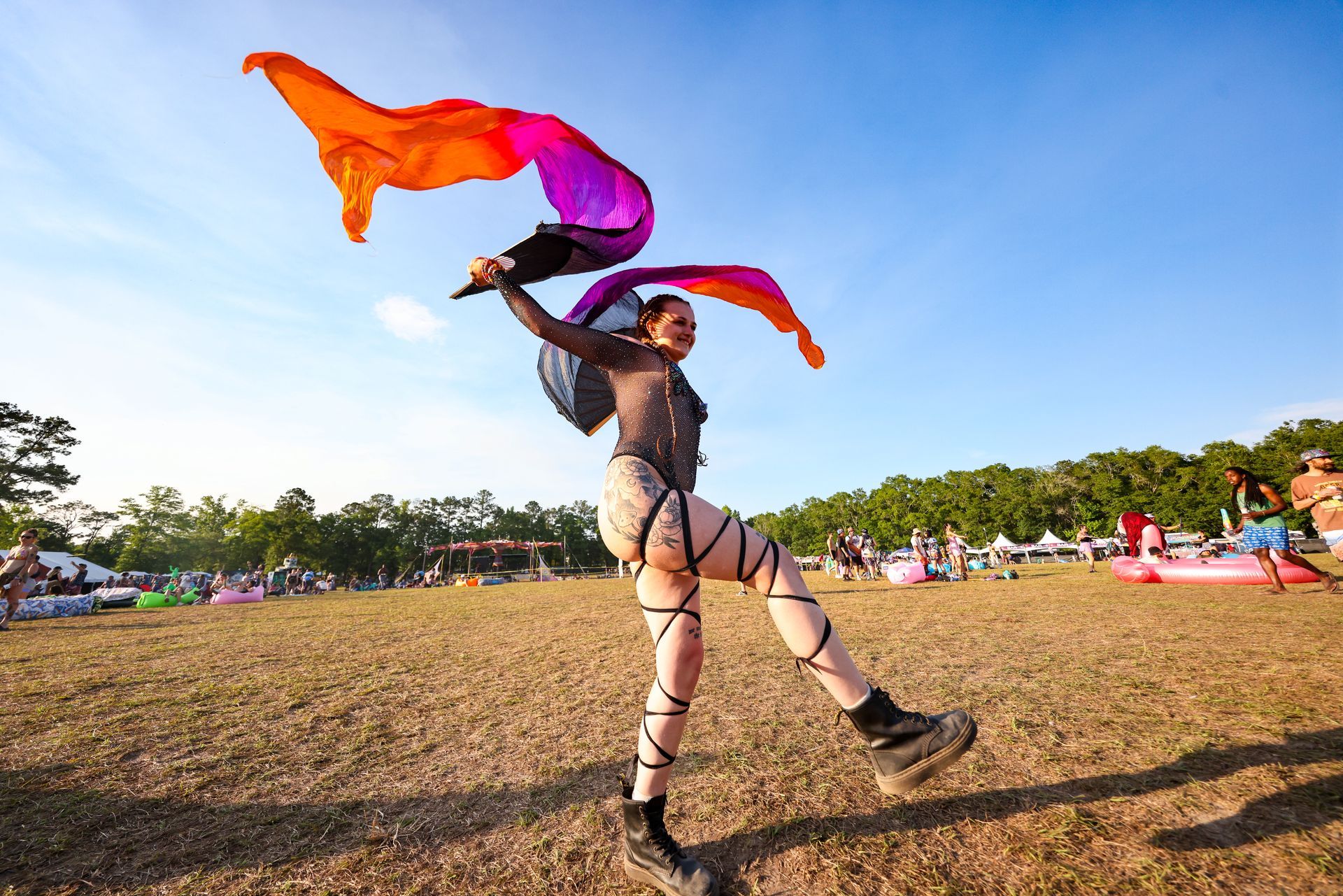 A woman is dancing in a field while holding a rainbow flag.